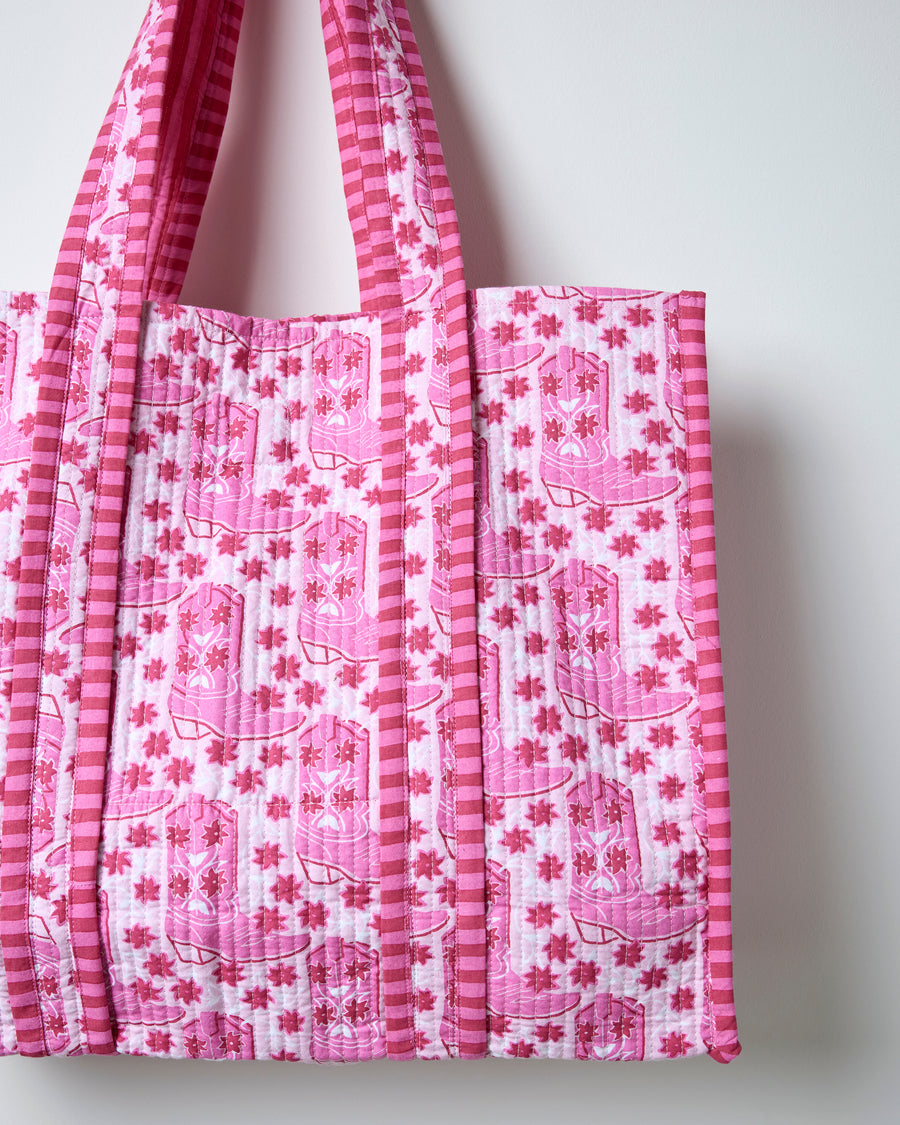Close view of the pink quilted traveler tote showing repeated western boot print, vertical quilting, and striped trim.