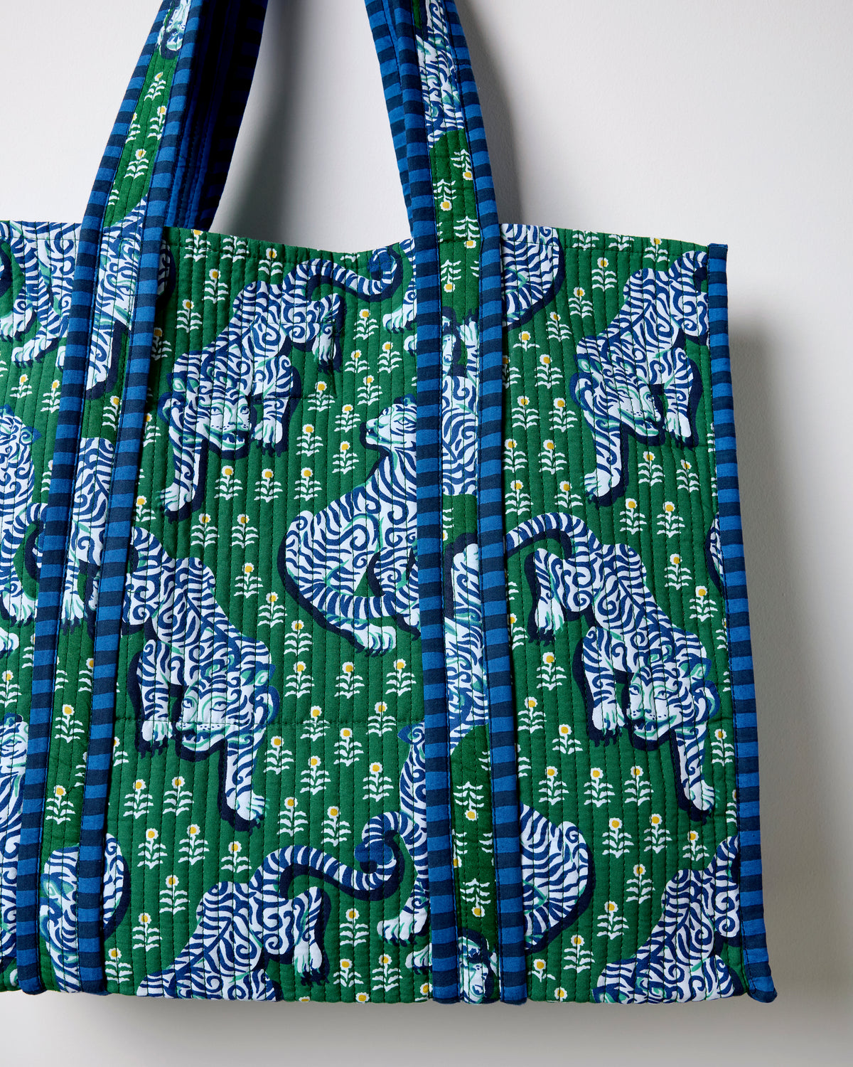 Close-up of the jade quilted tote showing the repeated blue-and-white tiger print, small white flowers, and striped handles and edging.