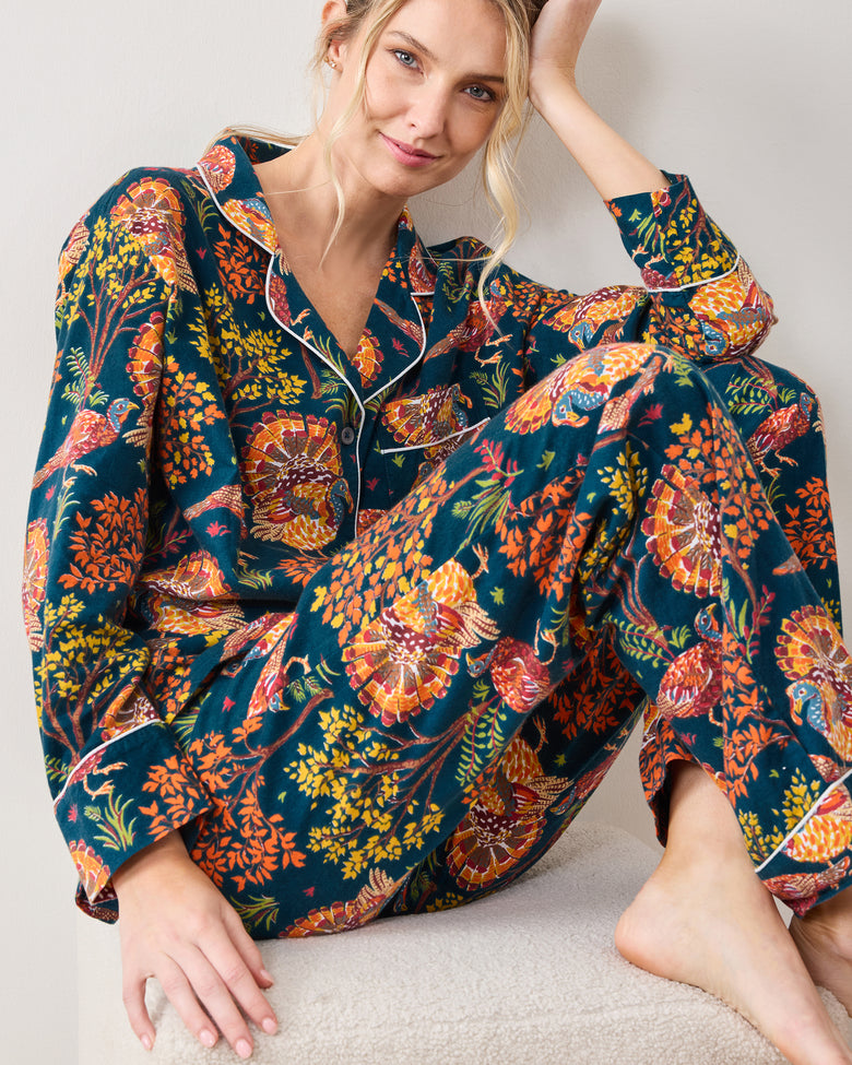 Close view of a model seated in the Turkey Trot navy pajama set, showing the piped collar, button front, pocket, cuffs, and printed pants.
