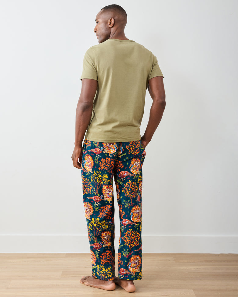 Back view of a model wearing the navy Turkey Trot long pajama pants with colorful turkey and autumn foliage print.