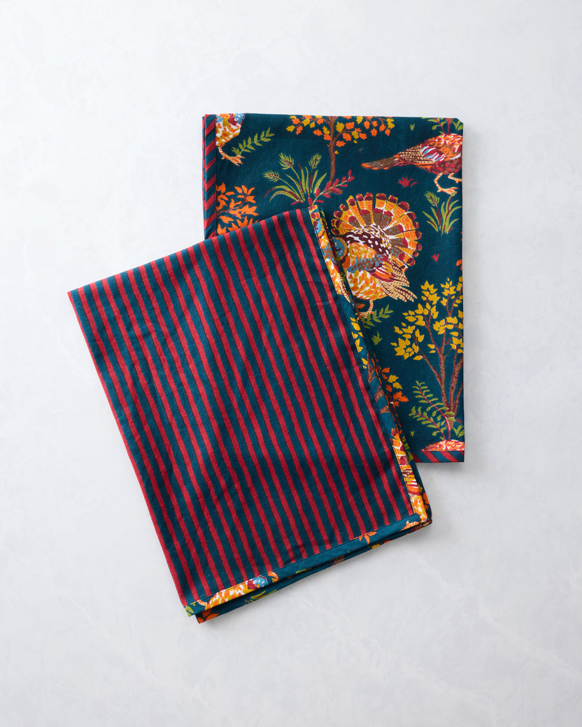Two folded navy tea towels showing a turkey and foliage print on one side and red-and-navy stripes on the other.