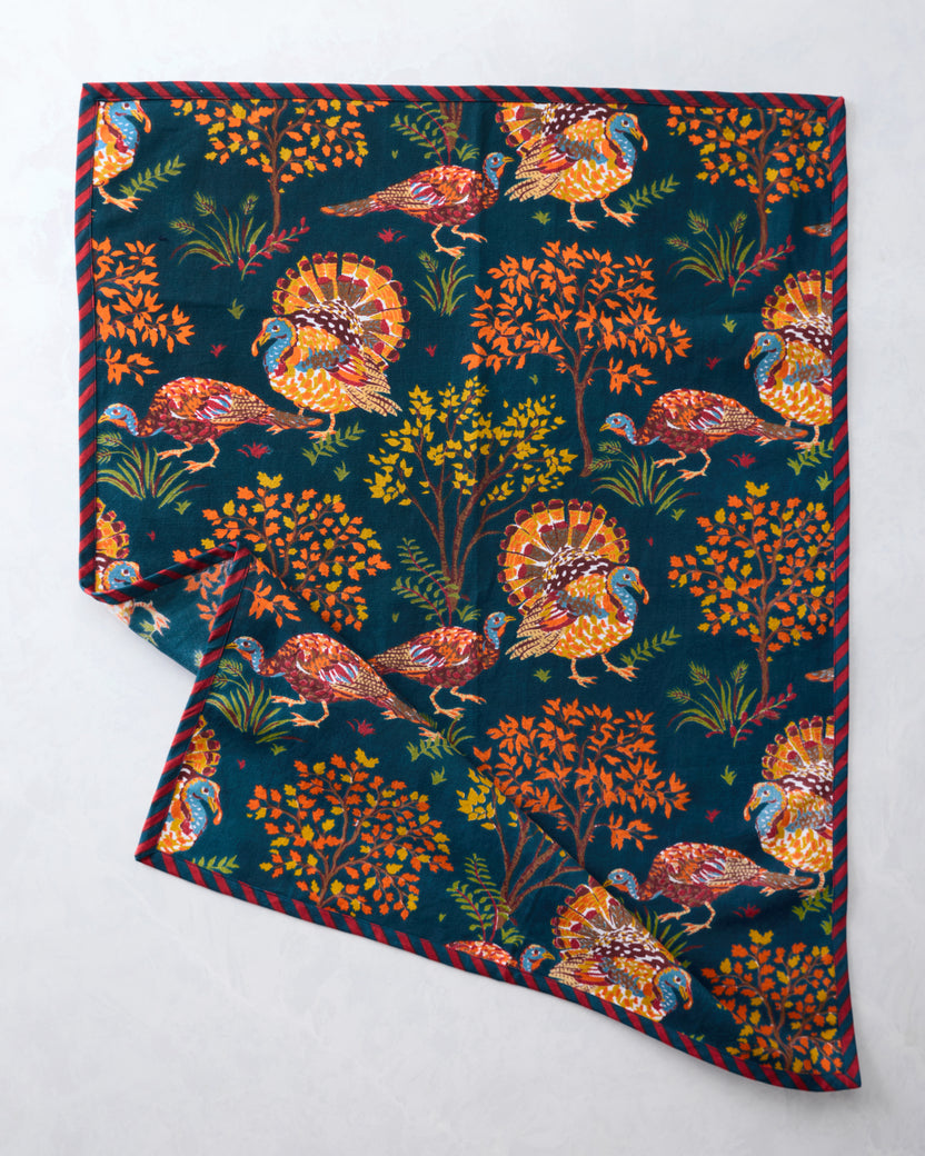 Navy tea towel spread flat with colorful turkey and autumn foliage print, with a corner folded back.