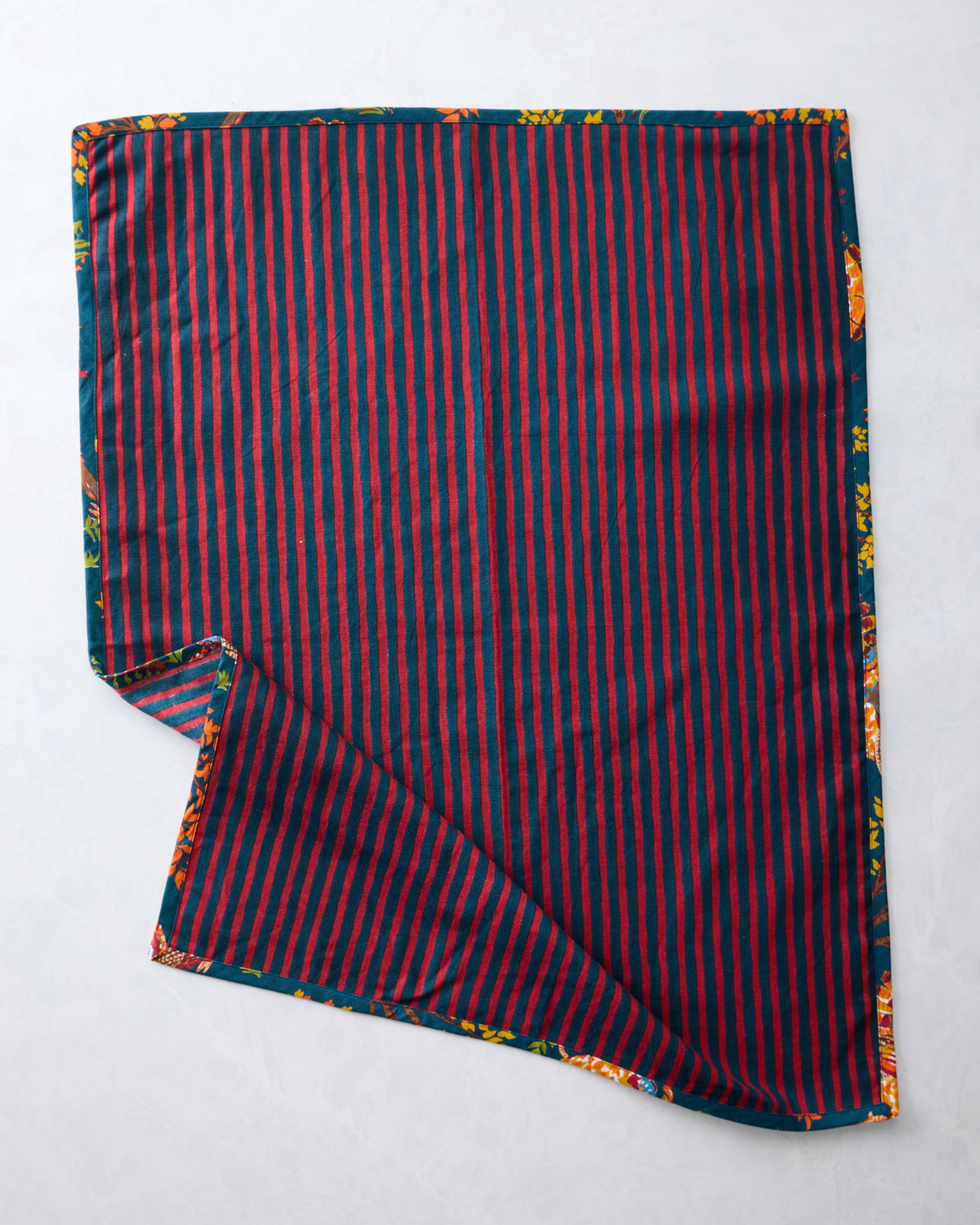 Tea towel showing a red-and-navy striped reverse side with a corner folded back to reveal the turkey print.