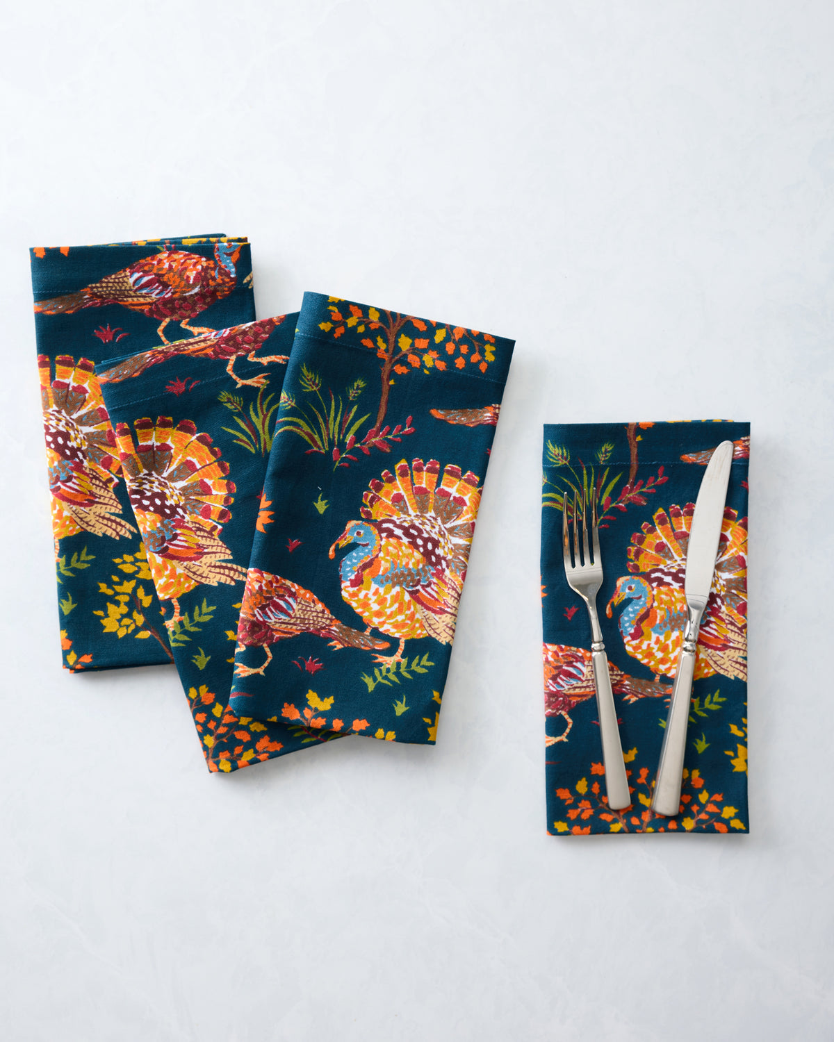 Four navy turkey-print dinner napkins arranged overlapping, with a fork and knife placed on one napkin.