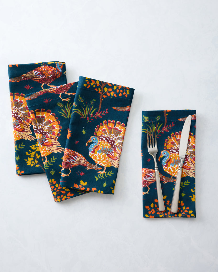Four navy turkey-print dinner napkins arranged overlapping, with a fork and knife placed on one napkin.