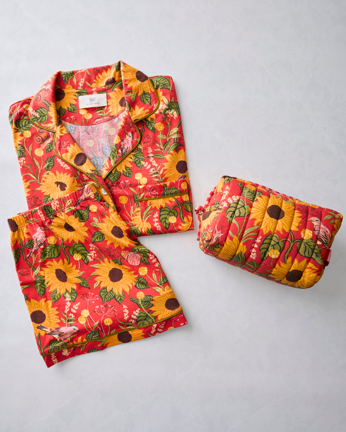 Red-orange short pajama set with sunflower print and matching quilted pouch.