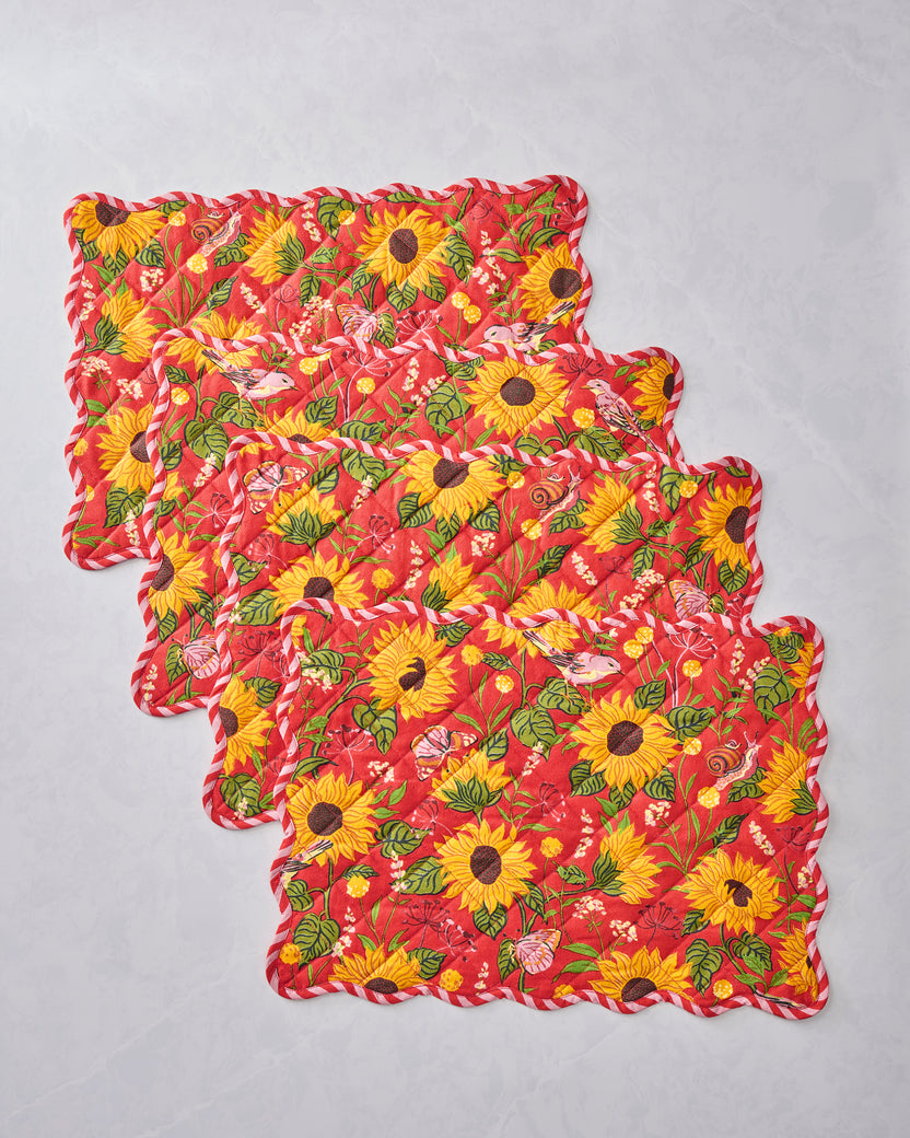 Four orange quilted placemats with scalloped edges and a sunflower-and-floral print, arranged in an overlapping stack.