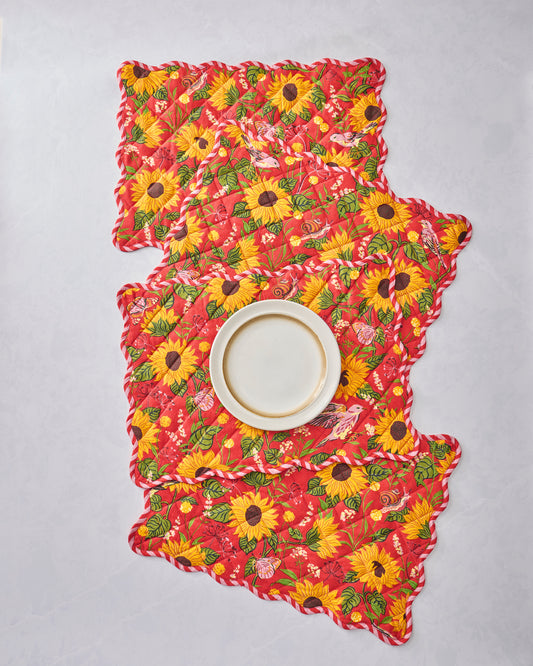 Four orange quilted placemats with scalloped edges and a sunflower, leaf, bird, and butterfly print, arranged beneath a white plate.