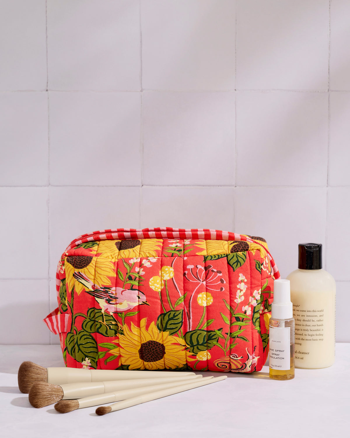 Orange quilted sunflower-print pouch shown with makeup brushes and bottles beside it.