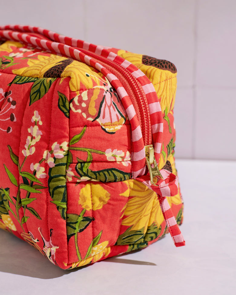 Close-up of the quilted pouch showing its orange floral print, pink-and-white striped trim, zipper, and gold-tone pull.