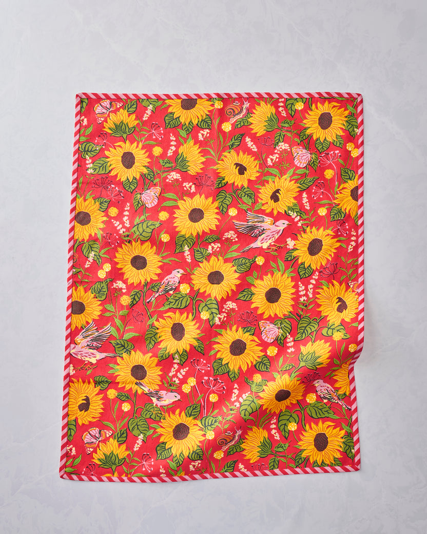 Tea towel displayed flat with an orange floral print featuring sunflowers, leaves, birds, butterflies, and a snail.