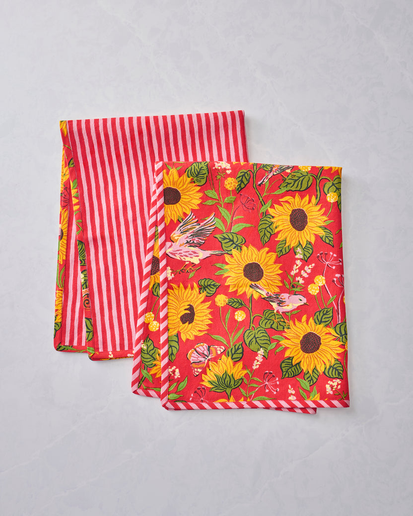 Two tea towels layered together, showing the orange sunflower print on one towel and the red-and-white striped side of the other.