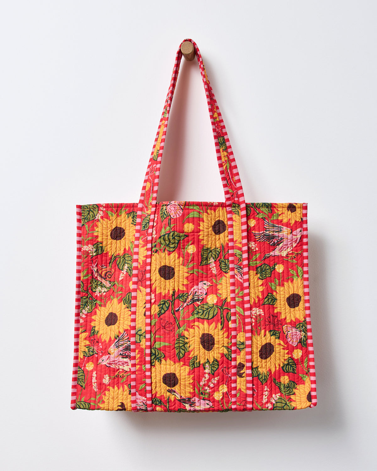 Front view of a red quilted traveler tote with sunflower, bird, butterfly, and floral print and striped handles.