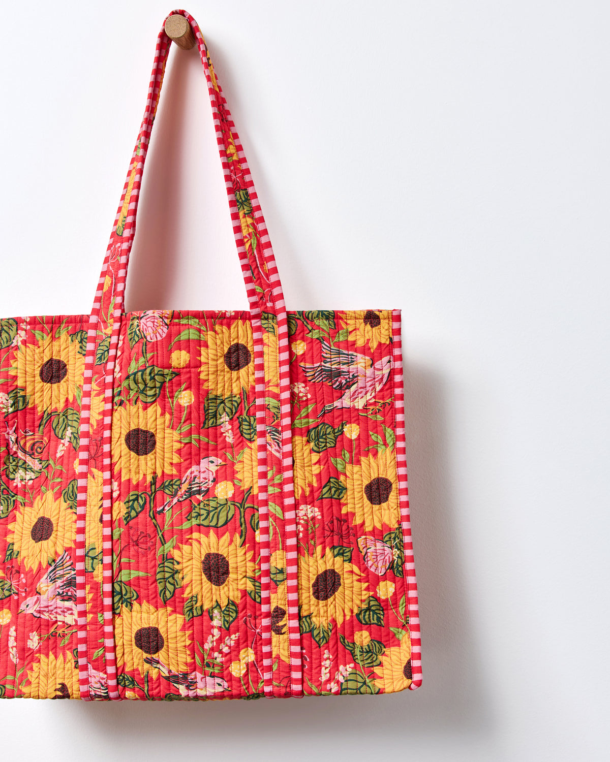 Close-up of the red quilted traveler tote showing its sunflower, bird, butterfly, and floral print and striped handles.