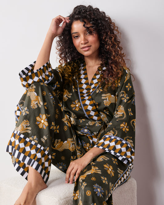 Seated close view of a person wearing the petite olive Bagheera Kaleidoscope wrap set, showing the wrap top, wide-leg pants, patterned cuffs, and waist tie.