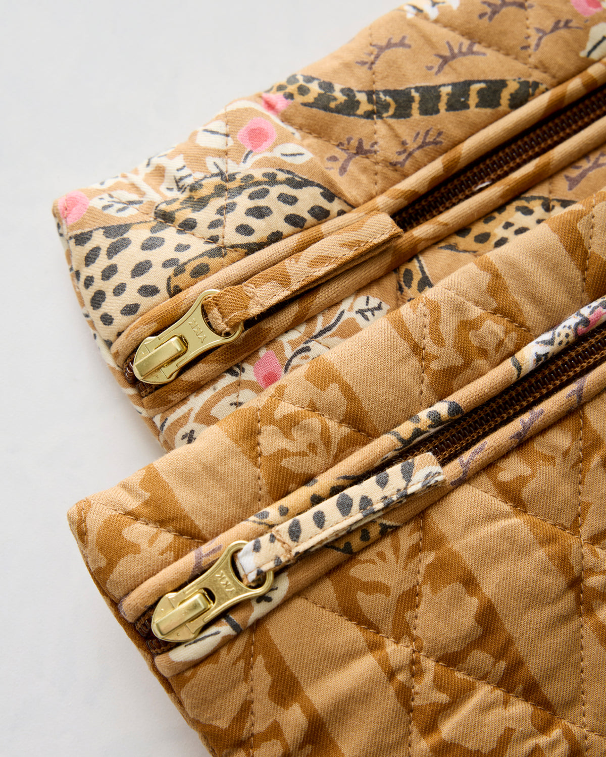 Close-up of two quilted pouches showing brown zippers, zipper pulls, and patterned trim.
