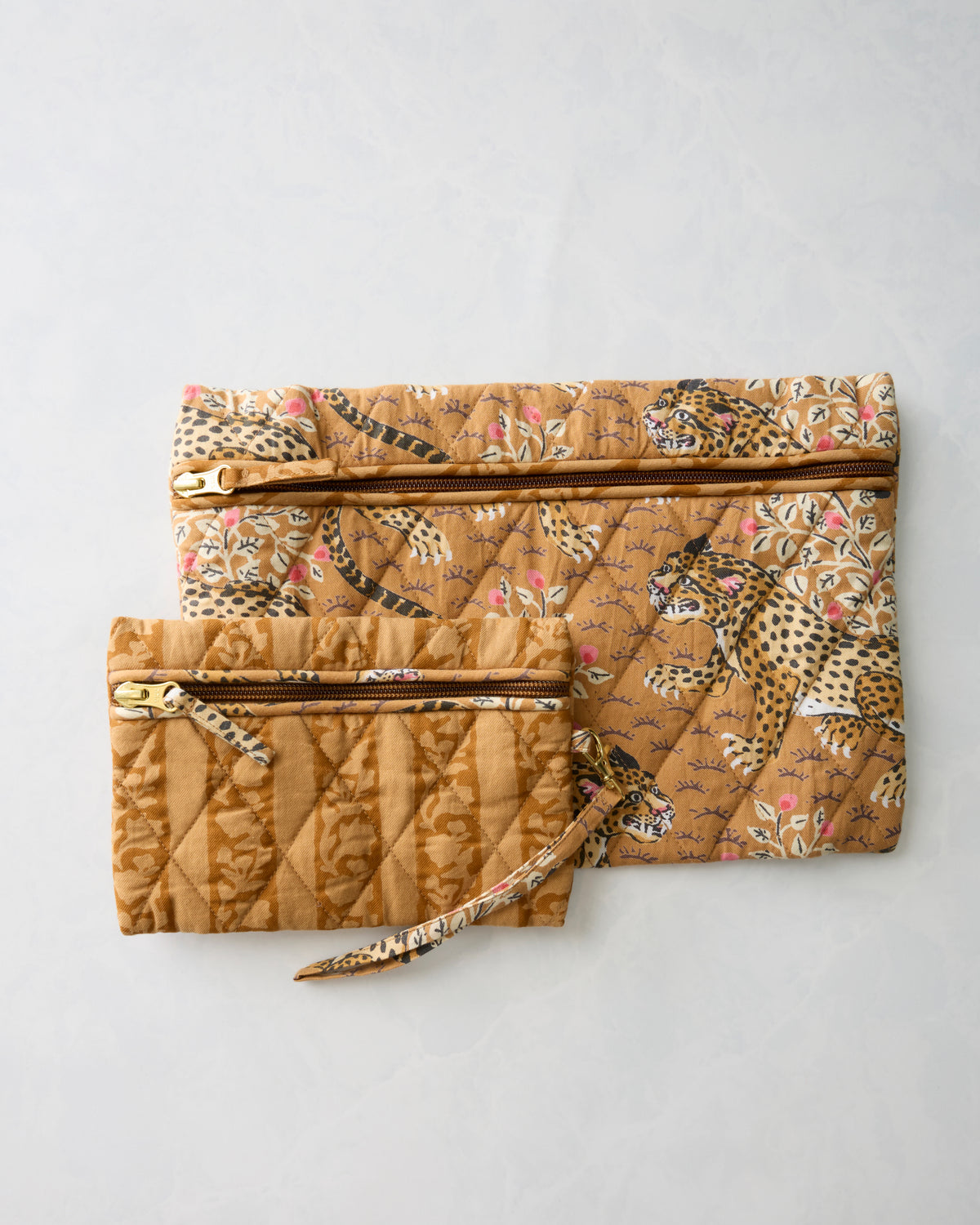 Two brown quilted zippered pouches overlapping, showing leopard and striped animal prints with wrist straps.