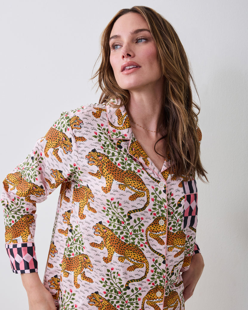 Close-up of a model wearing the Bagheera blush pajama top with leopard, jungle cat, foliage, and floral print, contrasting checkered cuffs and a chest pocket.