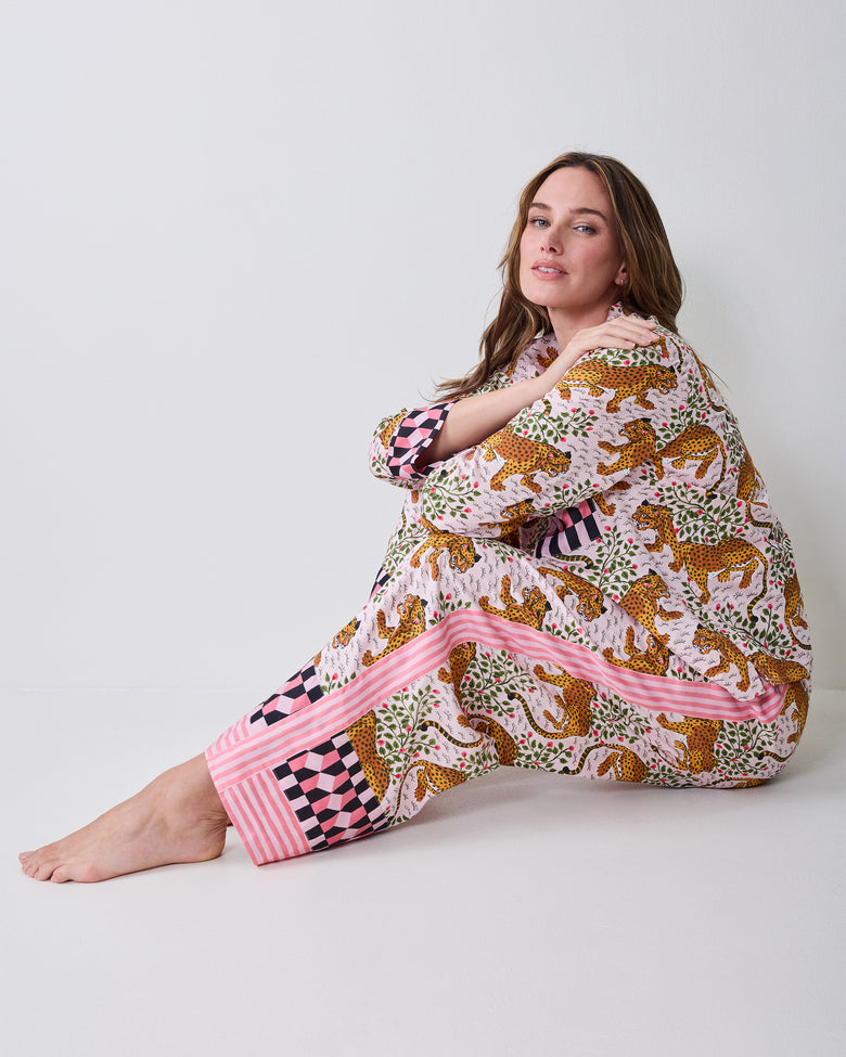 Model seated wearing the Bagheera tall blush pajama set, showing the printed top, wide-leg pants, and contrasting pink striped and checkered trim.