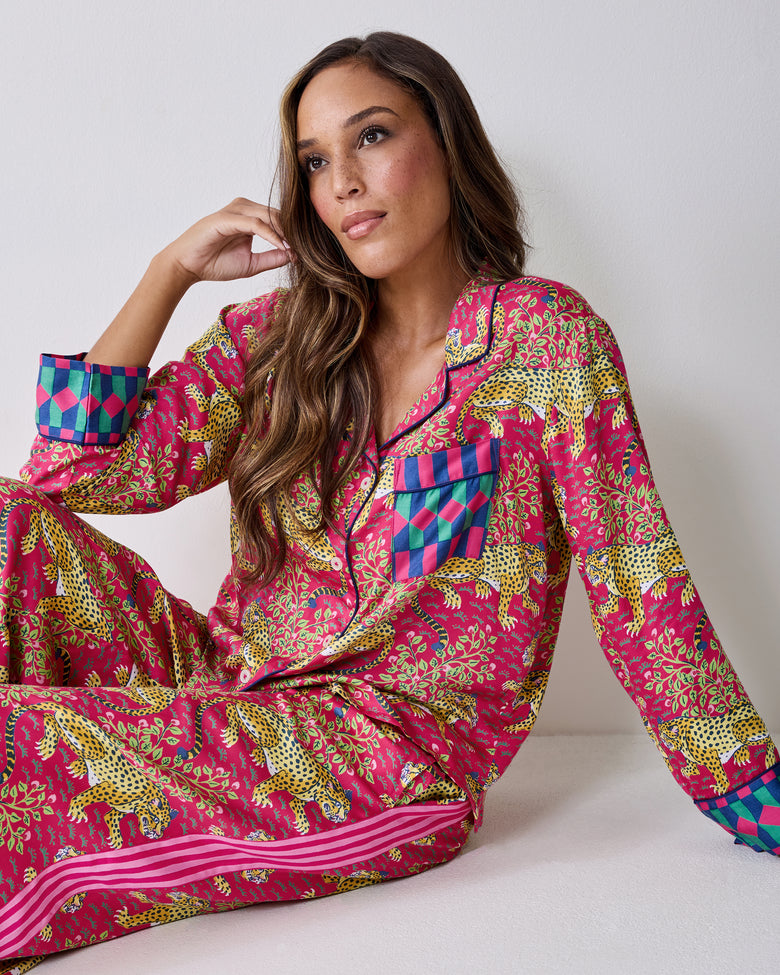 Seated view of the hot pink Bagheera pajama set with leopard-and-vine print, collared button-front top, chest pocket, and contrasting cuffs.