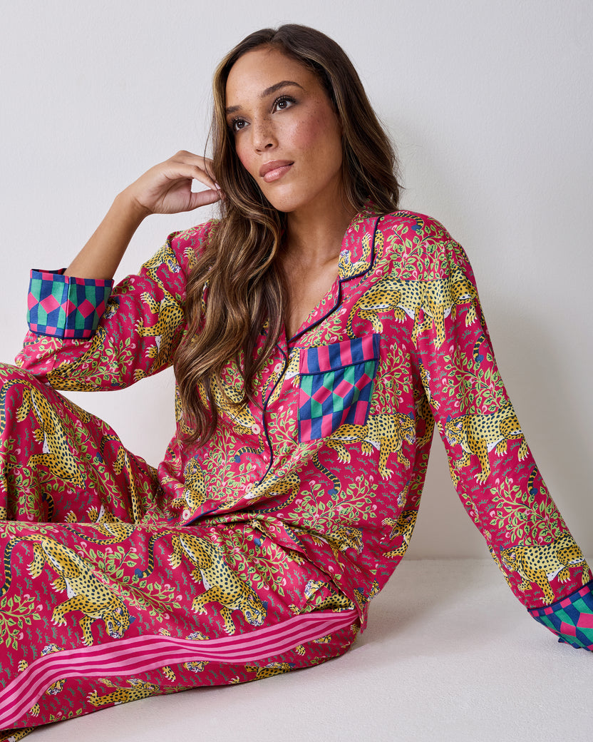 Seated view of the hot pink Bagheera pajama set with leopard-and-vine print, collared button-front top, chest pocket, and contrasting cuffs.