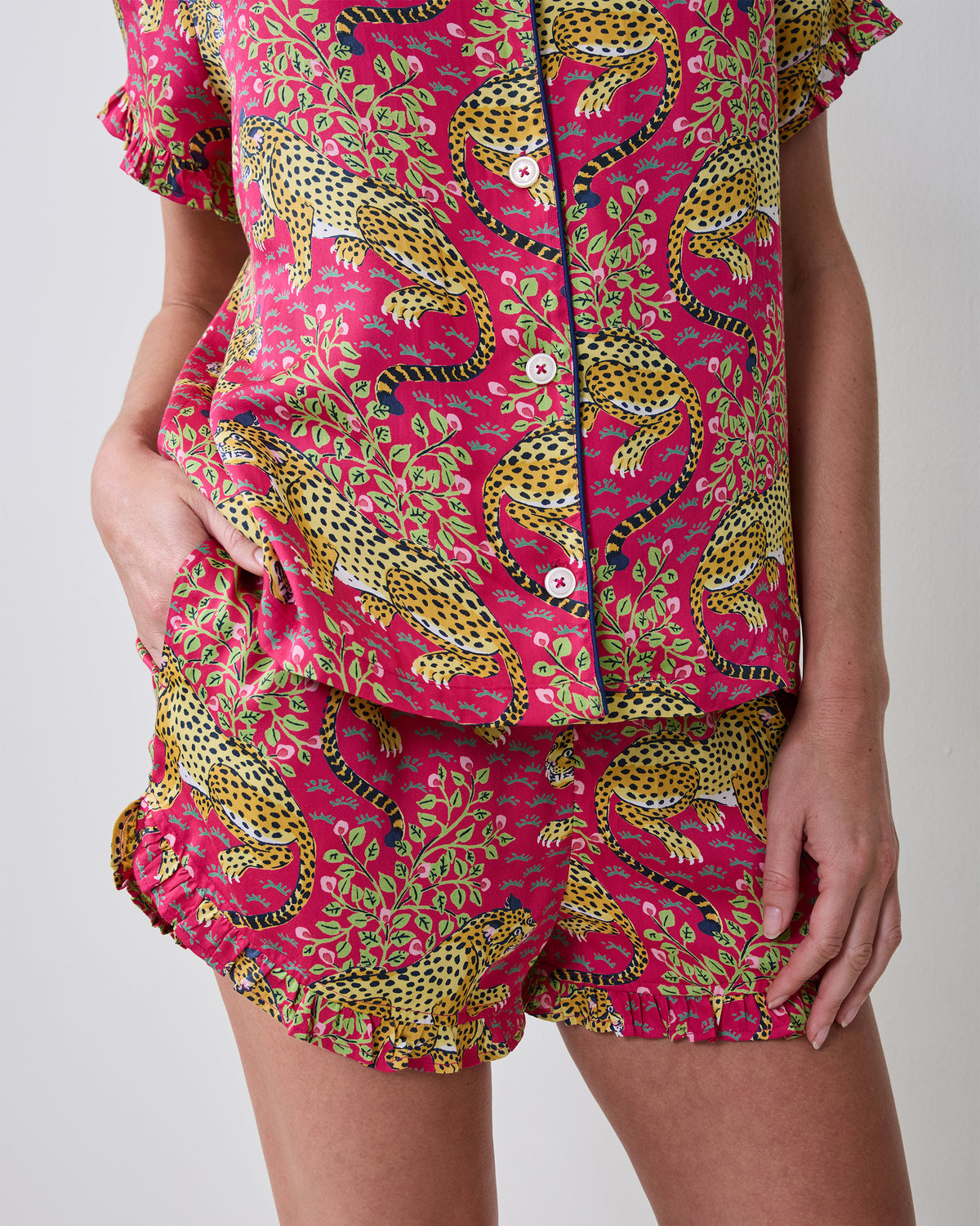 Close view of the hot pink Bagheera short pajama set, showing leopard print, button-front top, ruffled sleeves and hem, and shorts with a pocket.