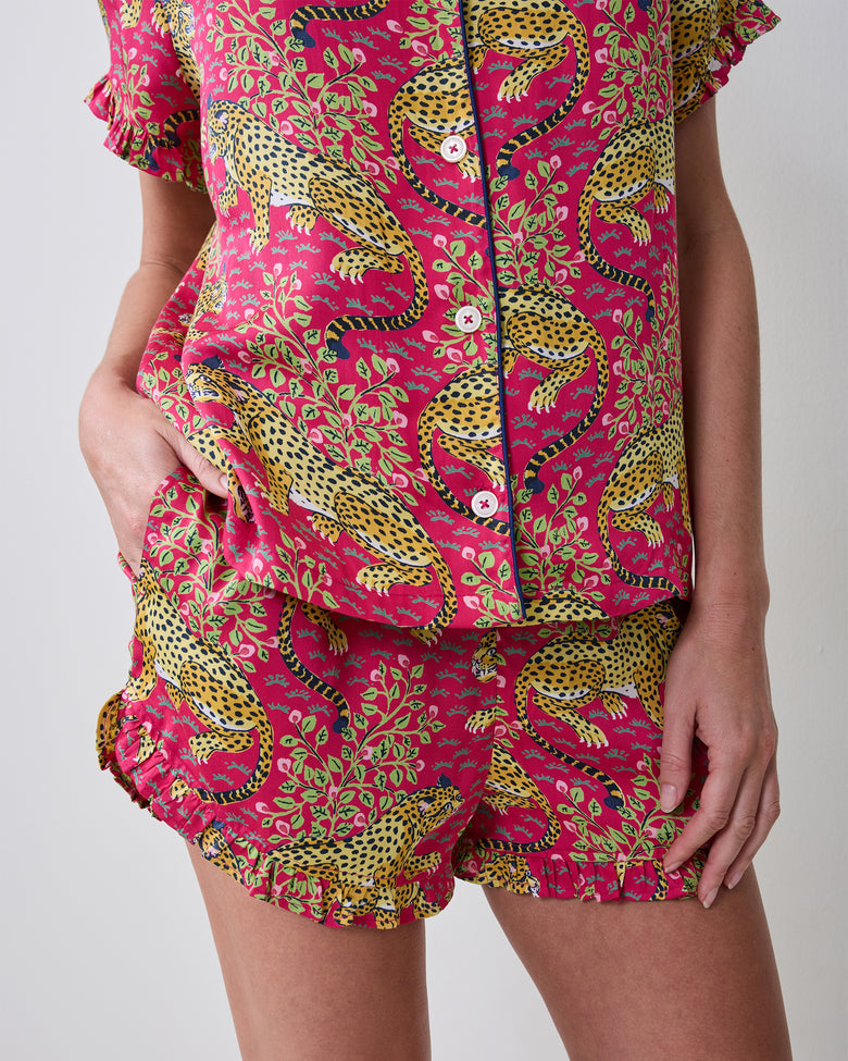 Close view of the hot pink Bagheera short pajama set, showing leopard print, button-front top, ruffled sleeves and hem, and shorts with a pocket.
