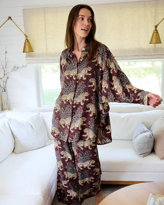 Person wearing the Raisin Bagheera Stevie pajama set with wide-leg pants, dolman sleeves, and a leopard print on a dark reddish-brown background.