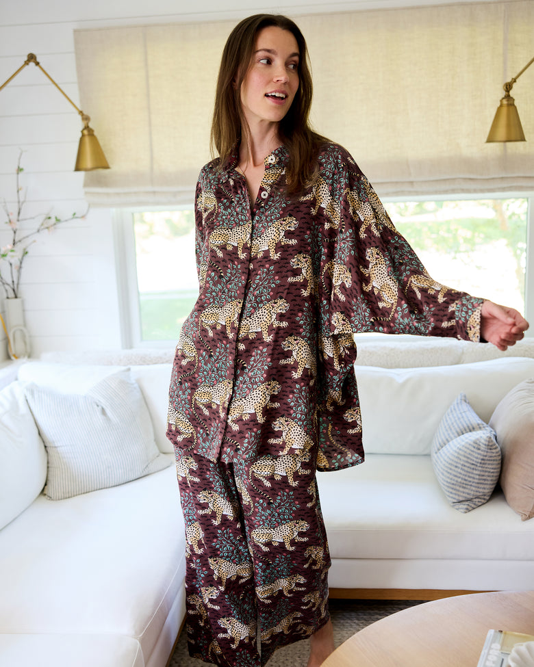 Person wearing the Raisin Bagheera Stevie pajama set with wide-leg pants, dolman sleeves, and a leopard print on a dark reddish-brown background.