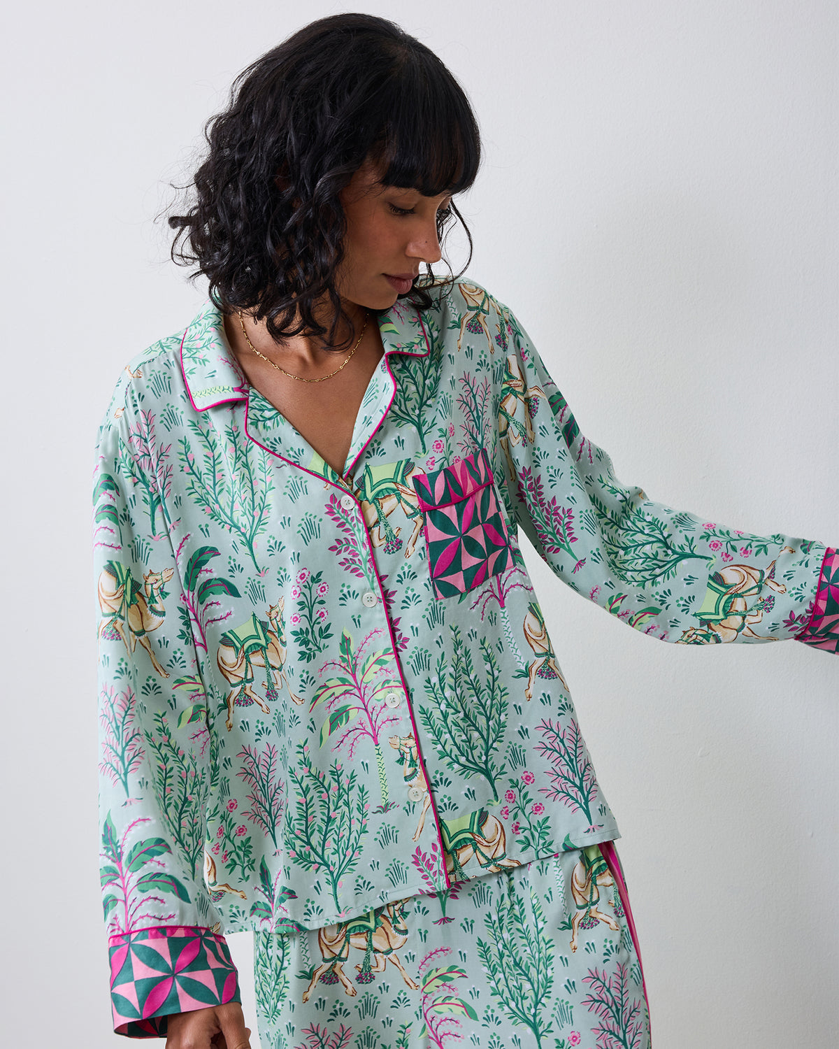 Close front view of the avocado Camel's Courtyard pajama top with long sleeves, camel-and-botanical print, pink piping, and a contrasting patterned chest pocket.