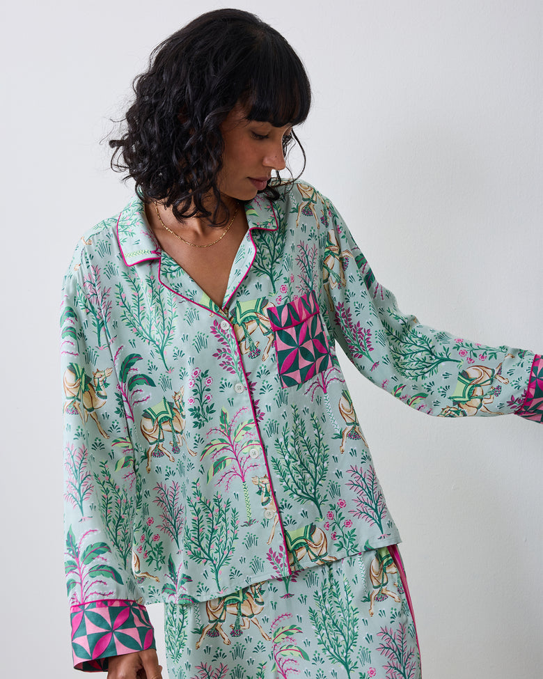 Close front view of the avocado Camel's Courtyard pajama top with long sleeves, camel-and-botanical print, pink piping, and a contrasting patterned chest pocket.
