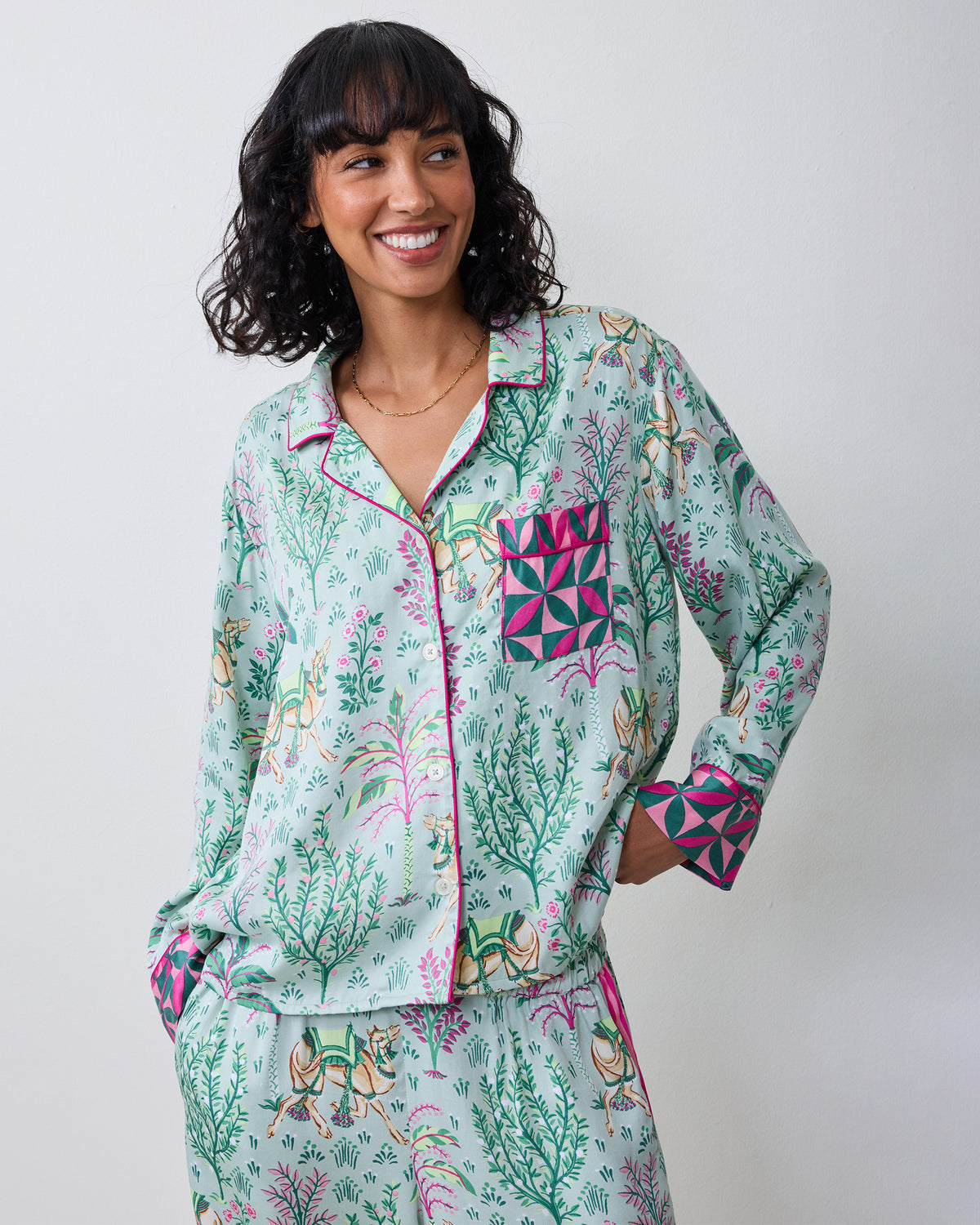 Front view of a model wearing the avocado Camel's Courtyard long-sleeve pajama set with a camel-and-botanical print, wide-leg pants, and contrasting patterned cuffs and pocket.