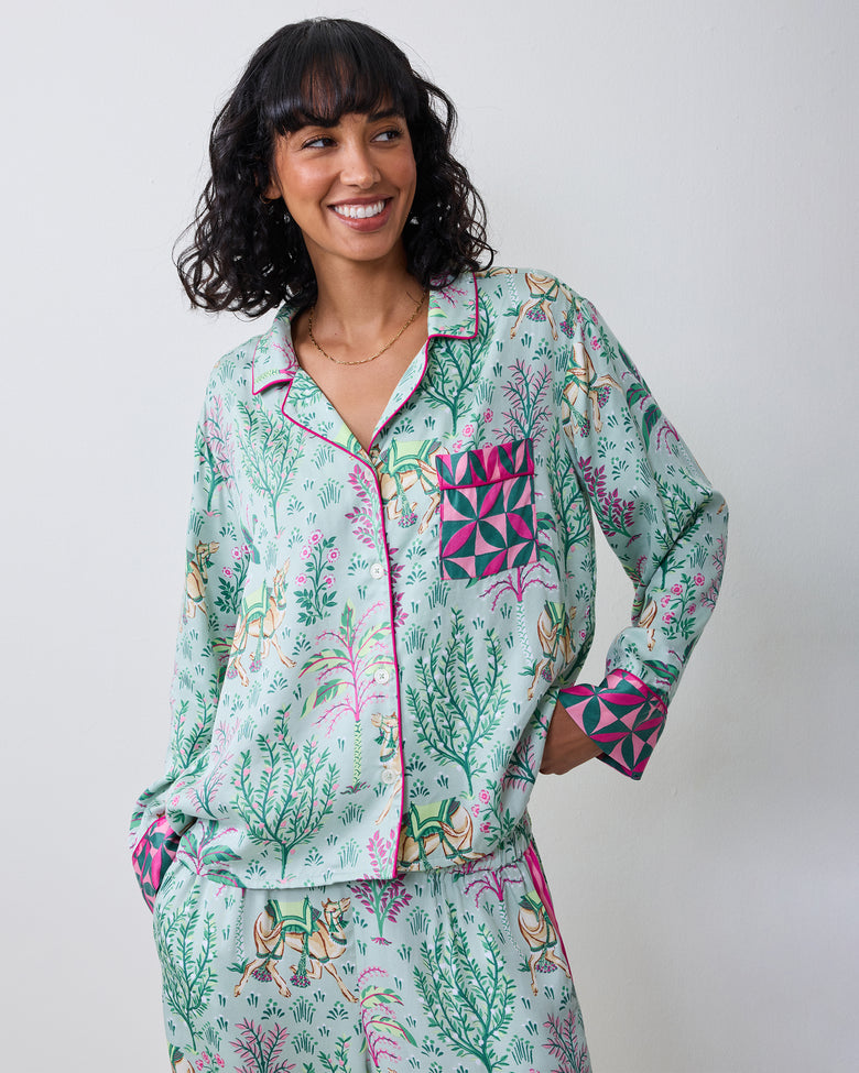 Front view of a model wearing the avocado Camel's Courtyard long-sleeve pajama set with a camel-and-botanical print, wide-leg pants, and contrasting patterned cuffs and pocket.
