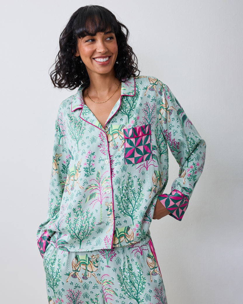 Front view of a model wearing the avocado Camel's Courtyard long-sleeve pajama set with a camel-and-botanical print, wide-leg pants, and contrasting patterned cuffs and pocket.