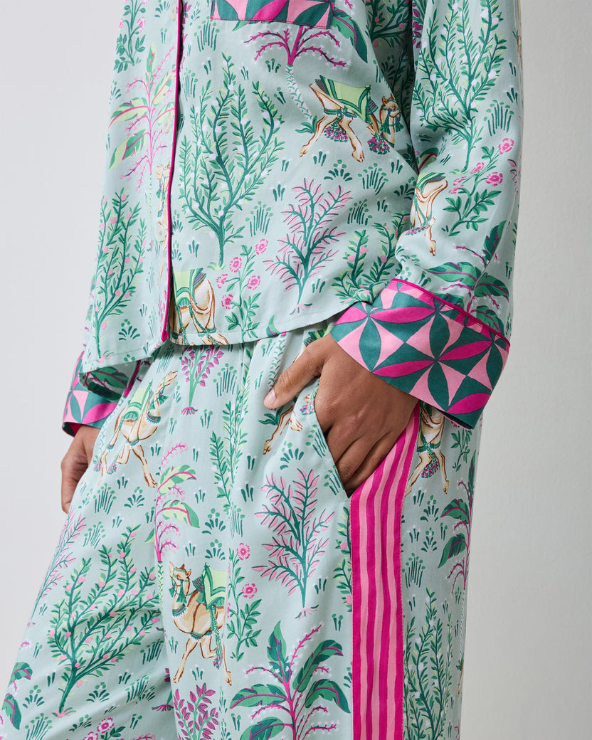 Close view of the avocado Camel's Courtyard pajama top and wide-leg pants, showing the camel-and-botanical print, contrasting cuff, side stripe, and pants pocket.