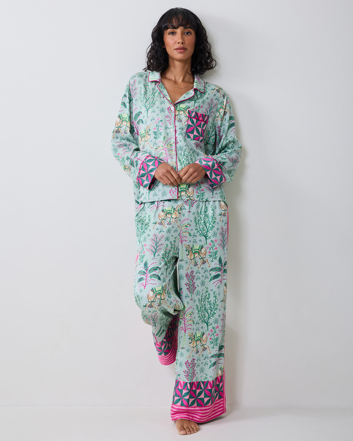 Model wearing the Avocado Camel's Courtyard petite pajama set with a botanical and camel print, shown standing with one leg raised.