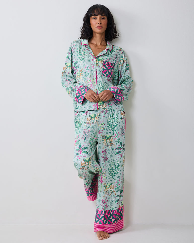Model wearing the Avocado Camel's Courtyard petite pajama set with a botanical and camel print, shown standing with one leg raised.
