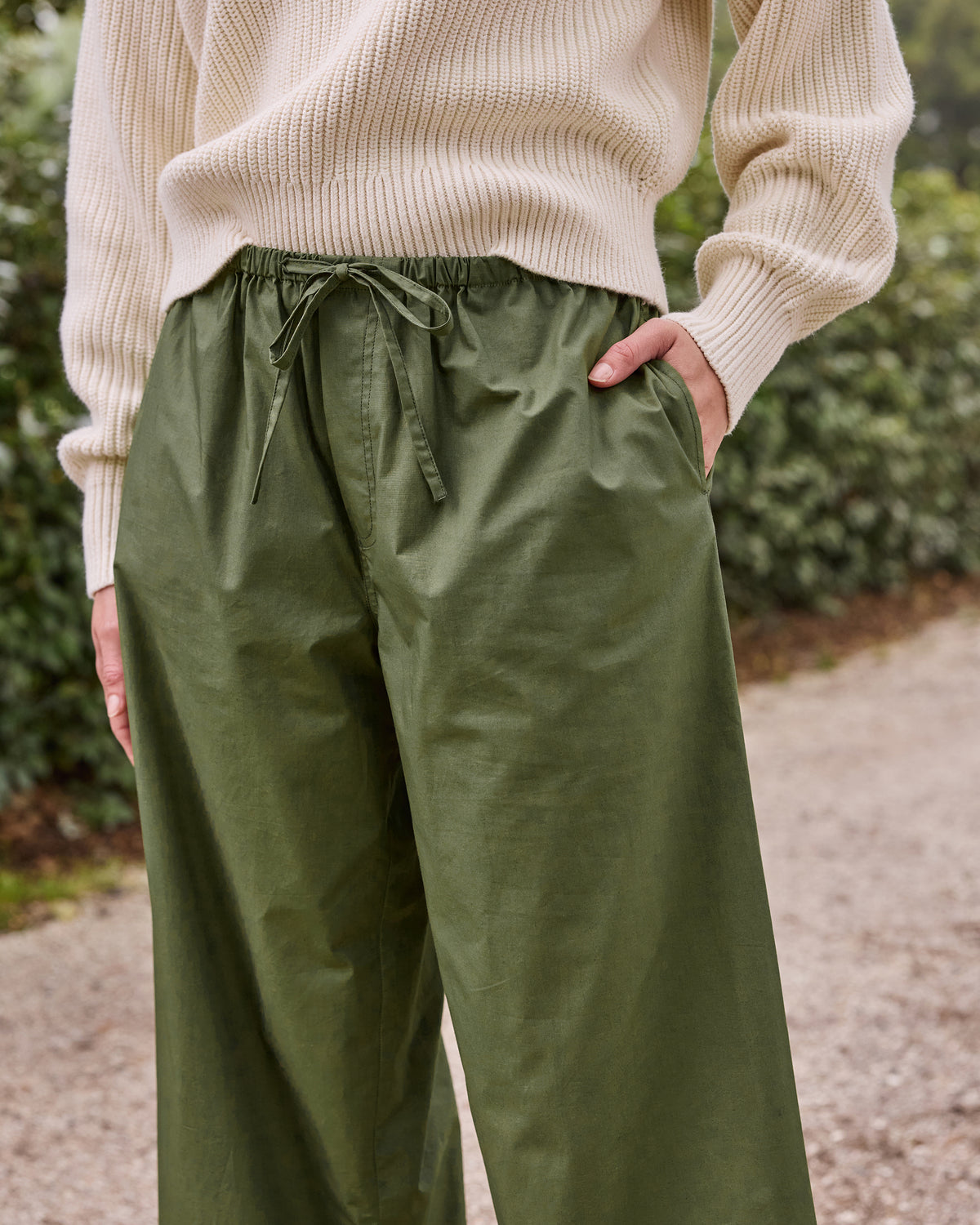 Close front view of olive pants showing the elastic drawstring waist and side pocket.