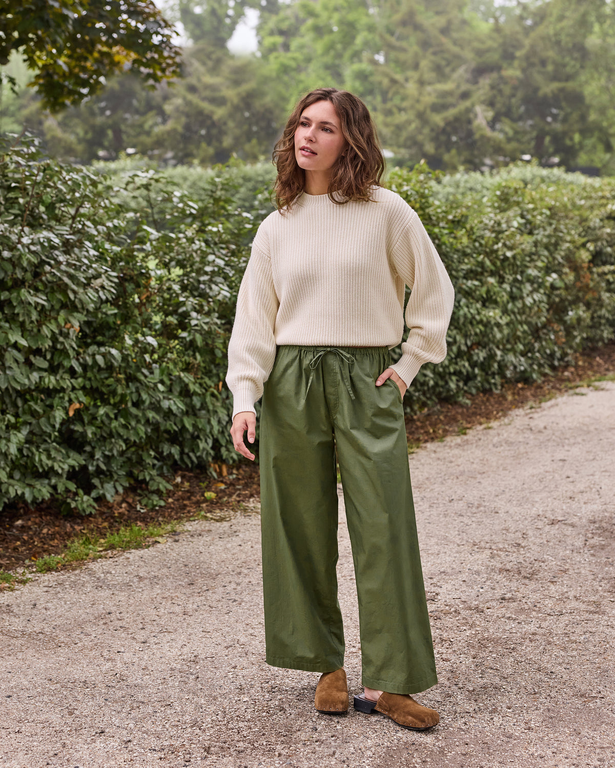 Three-quarter front view of olive wide-leg pants with a drawstring waist and side pockets, worn with a cream sweater.