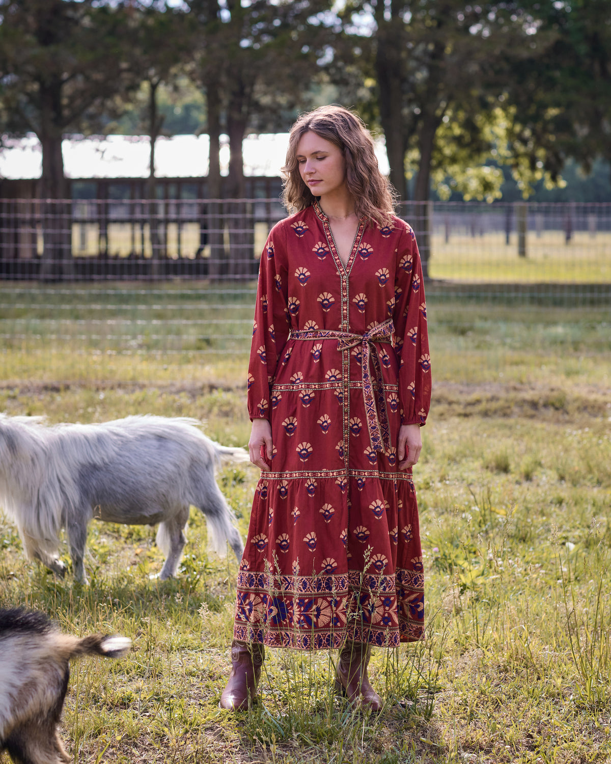 Front view of the Maybelle red patterned maxi dress with long sleeves, button-front opening, and waist belt, worn in a field.