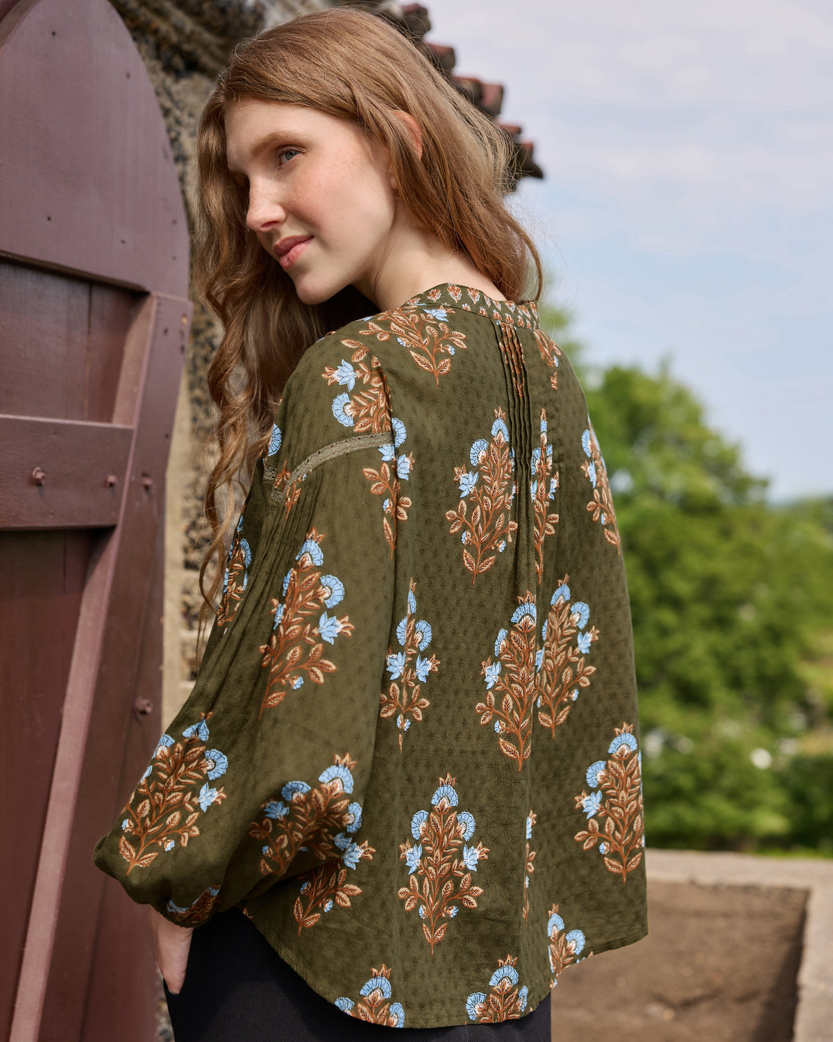 Back view of the deep olive Belmont blouse showing its floral print, pleated back, and long sleeves.