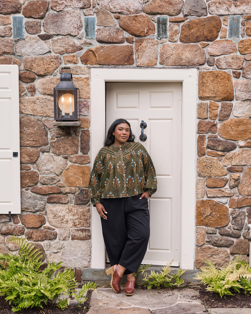 Full-length view of a model wearing the deep olive floral Belmont blouse with black pants.