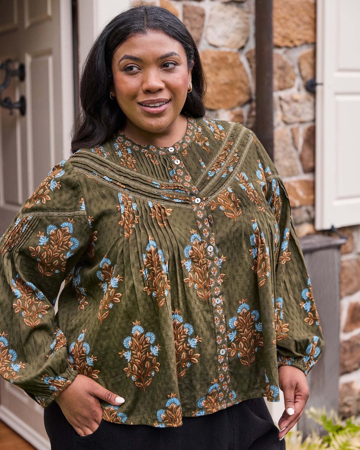 Close front view of the deep olive Belmont blouse showing its blue and brown floral print, pleated details, lace-trimmed yoke, and white buttons.