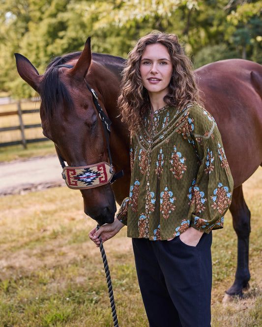 Colorado Wildflowers Belmont Blouse in deep olive with long sleeves and a floral print, shown beside a brown horse.