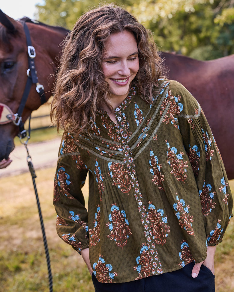 Model wearing the deep olive Belmont blouse with blue and brown floral print, pleated front, lace-trimmed yoke, and long sleeves.