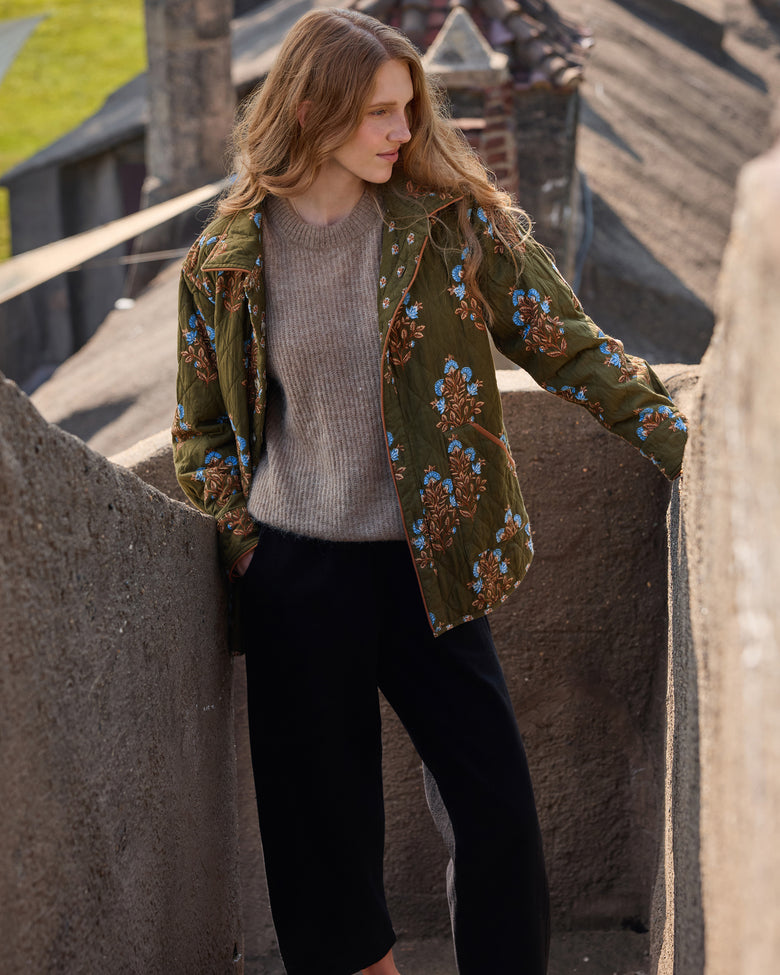 Model wearing the deep olive floral-print quilted jacket open over a sweater, front view.