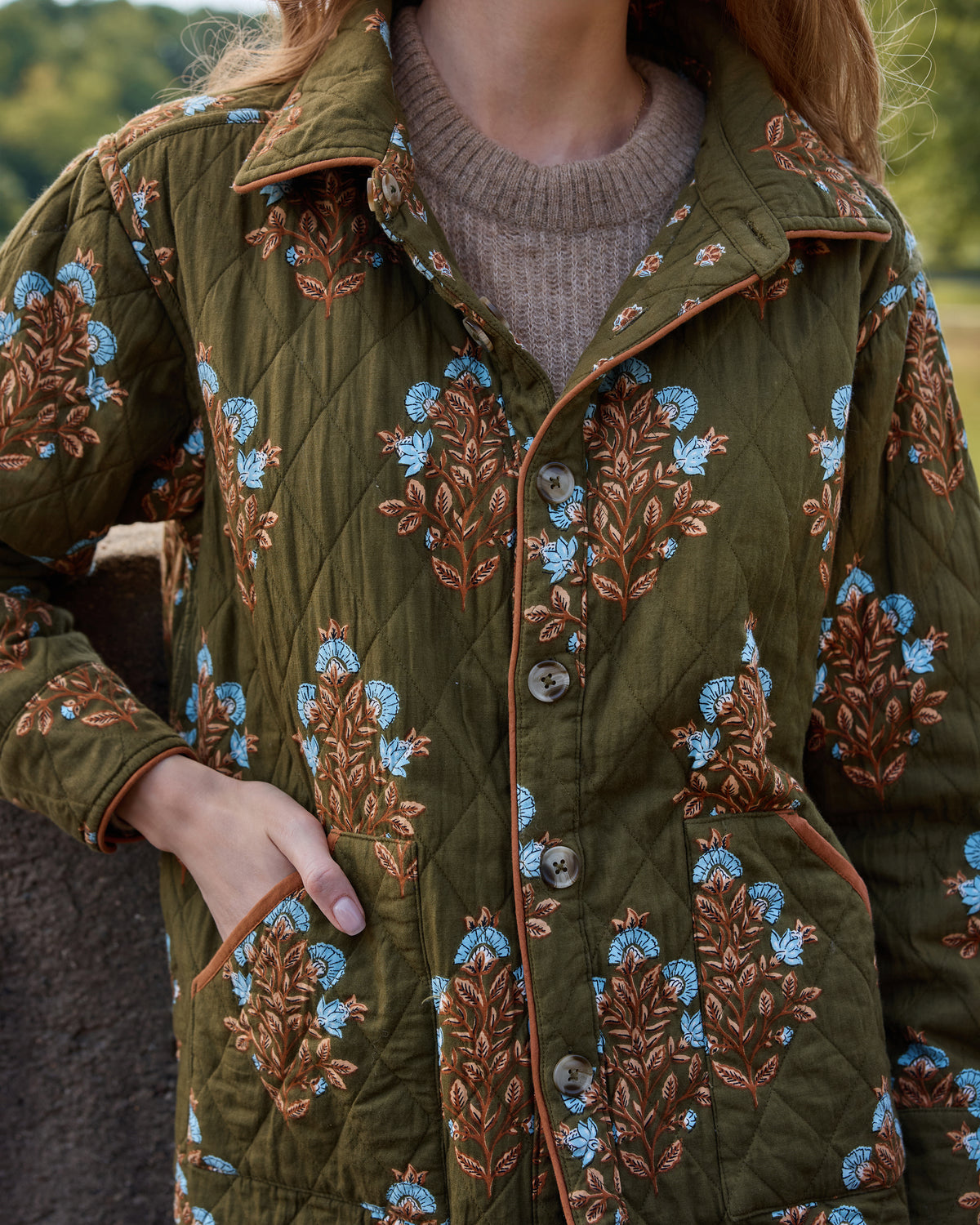 Close-up of the deep olive floral-print quilted jacket showing the collar, buttons, piping, and pockets.