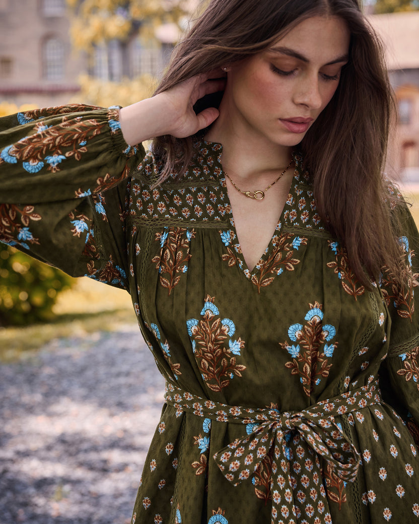 Close view of the deep olive Tallulah dress showing the V-neckline, patterned yoke, floral motifs, and tied waist sash.