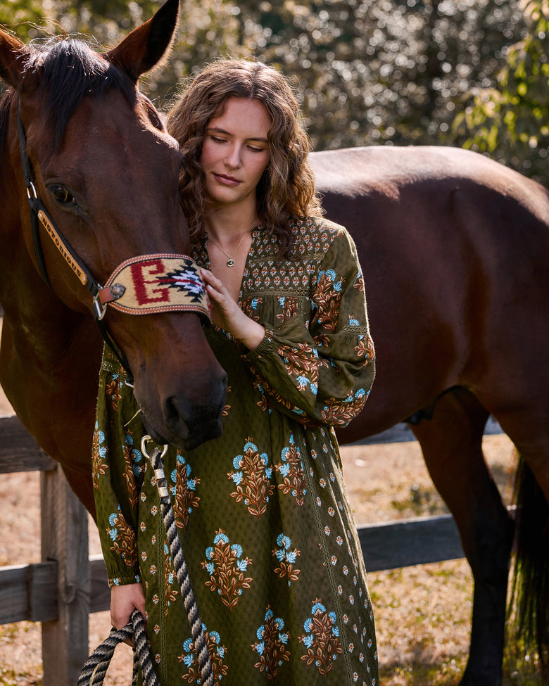 Colorado Wildflowers Tallulah Dress in deep olive with long sleeves and a floral print, shown beside a brown horse.