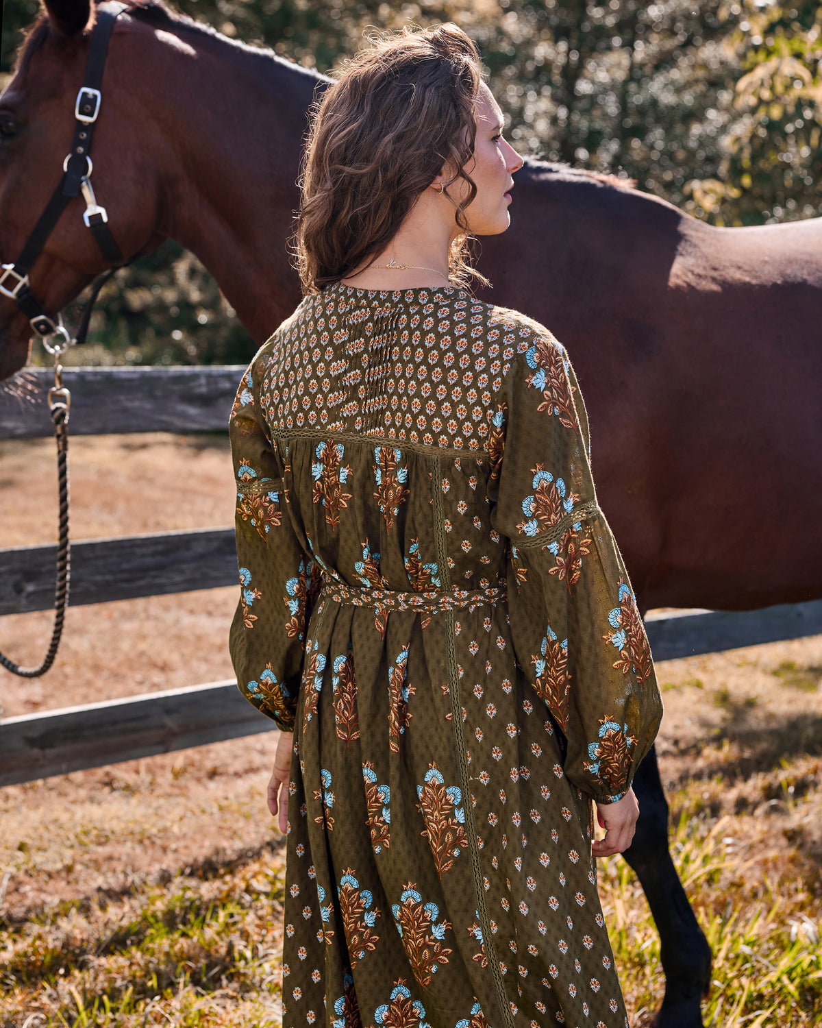 Back view of the deep olive Tallulah dress showing the patterned yoke, long sleeves, floral print, and waist sash.